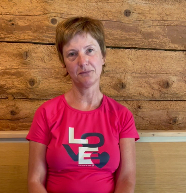 Frau im pinken Shirt mit „LOVE“-Aufdruck vor einer rustikalen Holzwand.