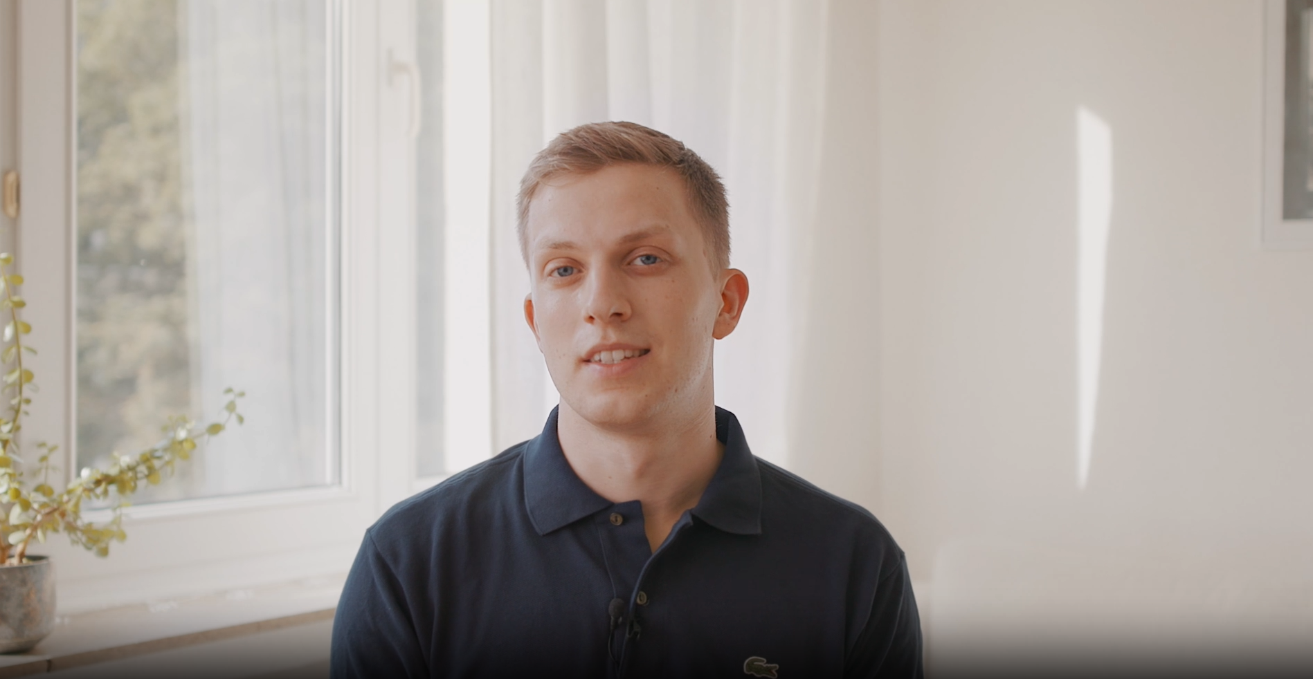 Mann im blauen Poloshirt blickt freundlich in heller, ruhiger Innenraumszene zur Kamera.